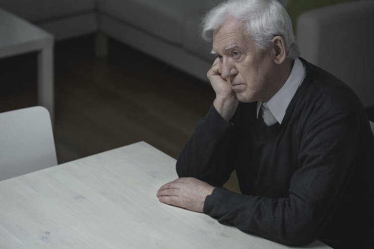Elderly man sitting at a table, looking tired and depressed.