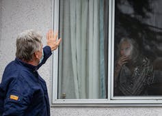 A man waves to an elderly woman through a window