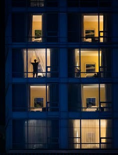 Outline of a person in one of several lit hotel windows, closing the curtains.