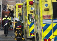 A paramedic carrying disinfectant walks past a row of ambulances