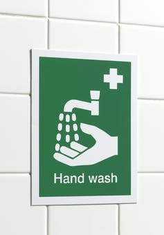 A green hand washing sign on a tile wall.