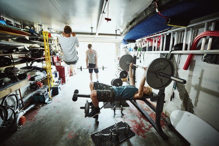 Three teenage boys lift weights together in a gym in a garage
