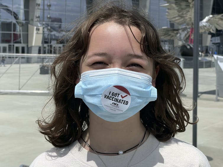 A 12-year-old girl wearing a face mask with a sticker reading 'I got vaccinated'