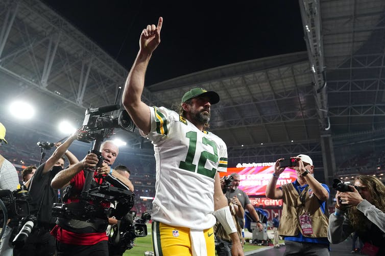 Green Bay Packers quarterback Aaron Rodgers leaving the field giving the No. 1 sign, with photographers behind him