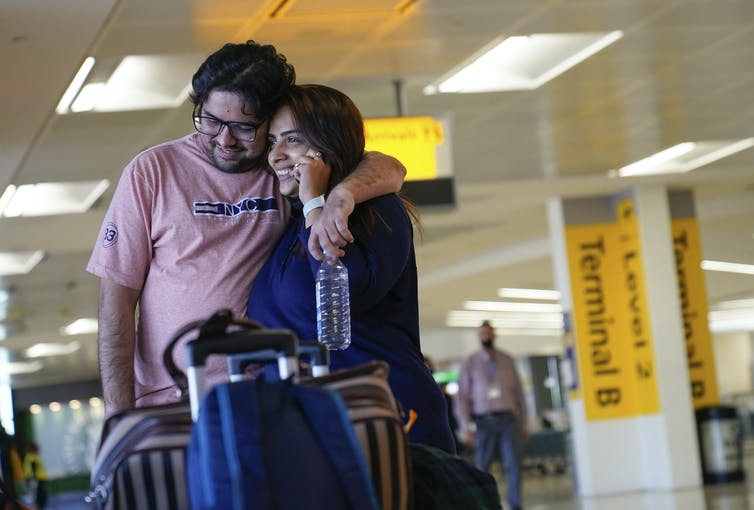A man and woman embrace as she talks on a cellphone in an airport.