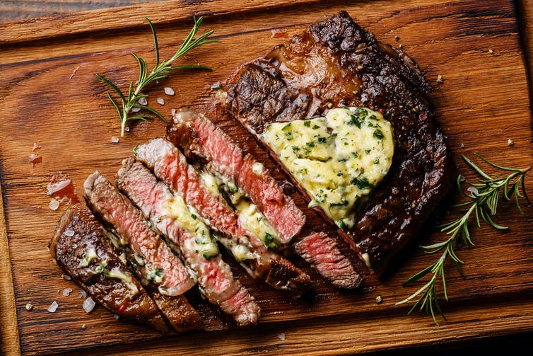 A medium-rare steak, sliced up on a wooden board and covered in butter.