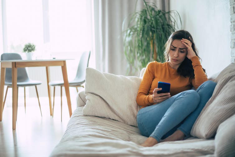 Woman with a frustrated expression looking at her smartphone while sitting on couch at home.