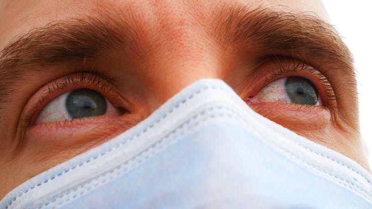 Close up of a man's irritated eyes, wearing a protective face mask