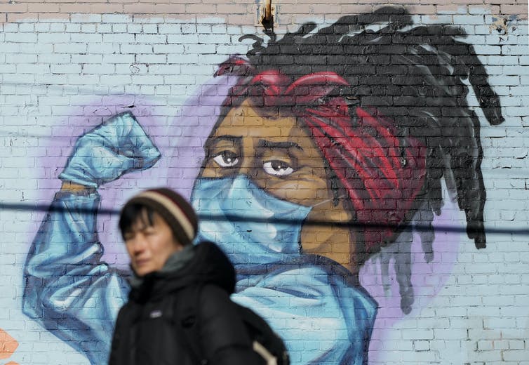 A person walks past a street mural of a health-care worker in PPE flexing a bicep