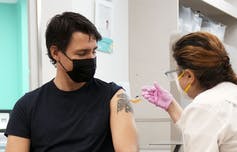 Justin Trudeau in a black T-shirt with his sleeve rolled up getting vaccinated.