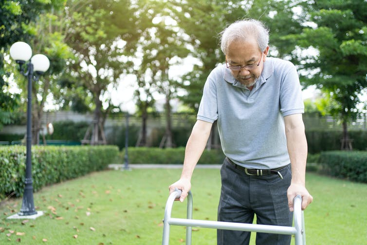An older man using his walker to walk outside.