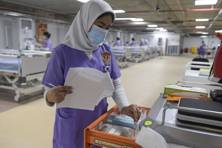 Health care worker wearing a headscarf looking through a medical supply drawer in an ICU.