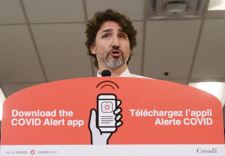 Prime Minister Justin Trudeau speaking at a podium that advertises a COVID Alert app.