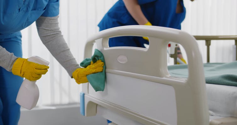 two people in scrubs disinfecting a hospital bed and room