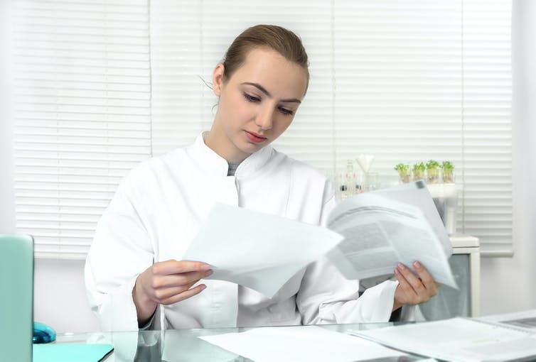 Young woman wearing a lab coat reviews some research papers.