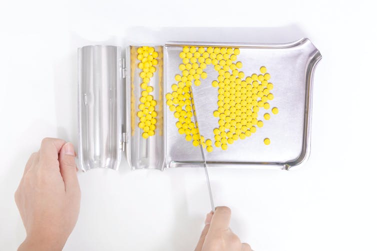Hands holding a pharmacist's tray filled with yellow pills