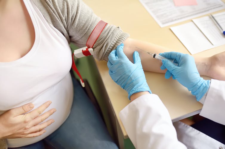 Cropped image of a pregnant woman with one hand on her belly while a health-care worker prepared to draw blood from her other arm