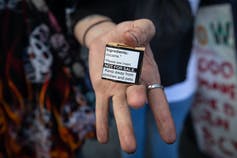 A hand holding a small box labelled 'Ingredients: Cocaine. Please see insert. NOT FOR SALE. Keep away from children and pets.'