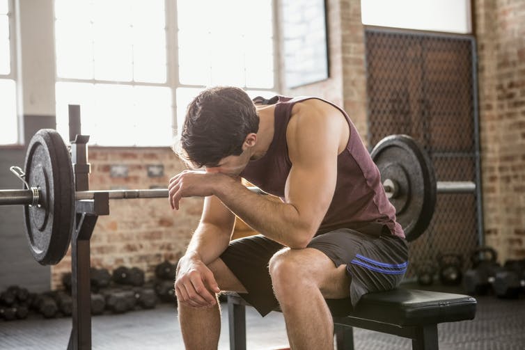 Young man sitting on bench press machine wipes away sweat after his workout.
