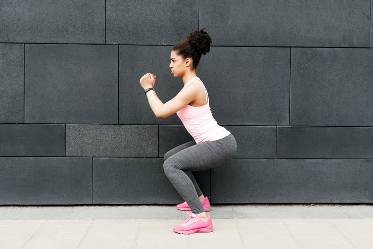 A woman in athletic wear performs a squat.