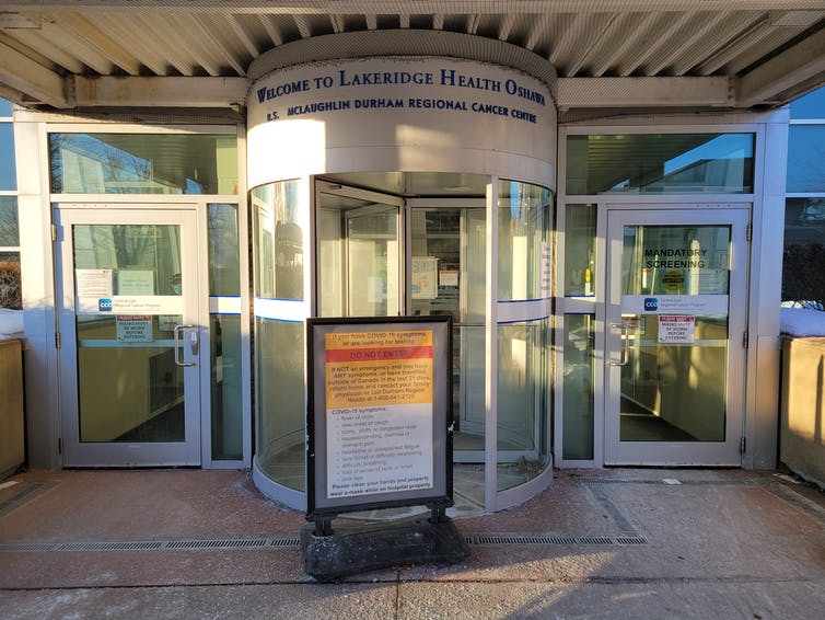 The entrance to a building with a revolving door and a sign in front stating COVID-19 protocols