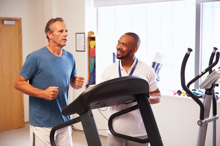 A man on a treadmill with a trainer beside him