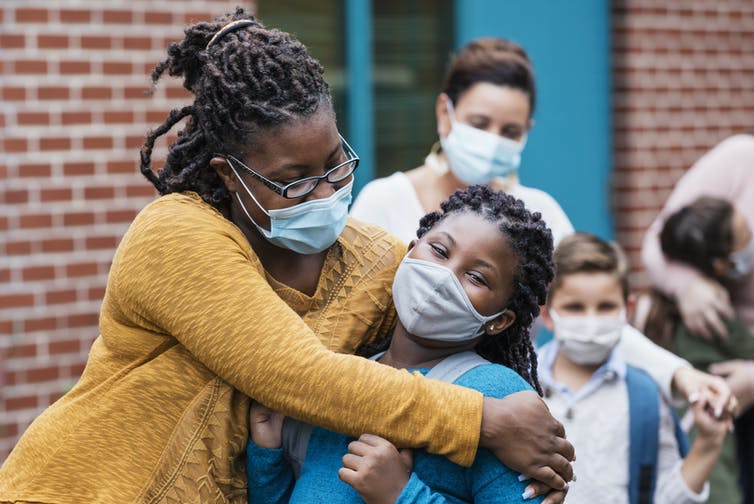 masked Black woman hugs masked elementary school girl