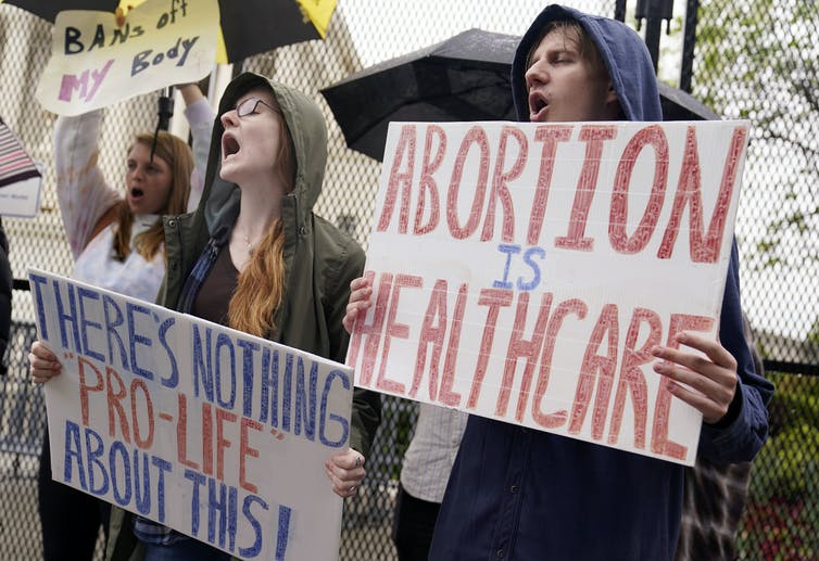 People holding signs reading 'There's nothing pro-life about this' and 'Abortion is healthcare'