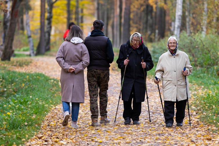 Two elderly ladies wearing winter coats stroll down a woodland path using walking poles.