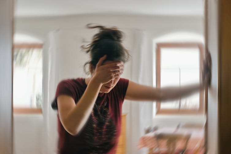 woman holding herself against a wall with one hand and her head with the other while she appears to be having a seizure