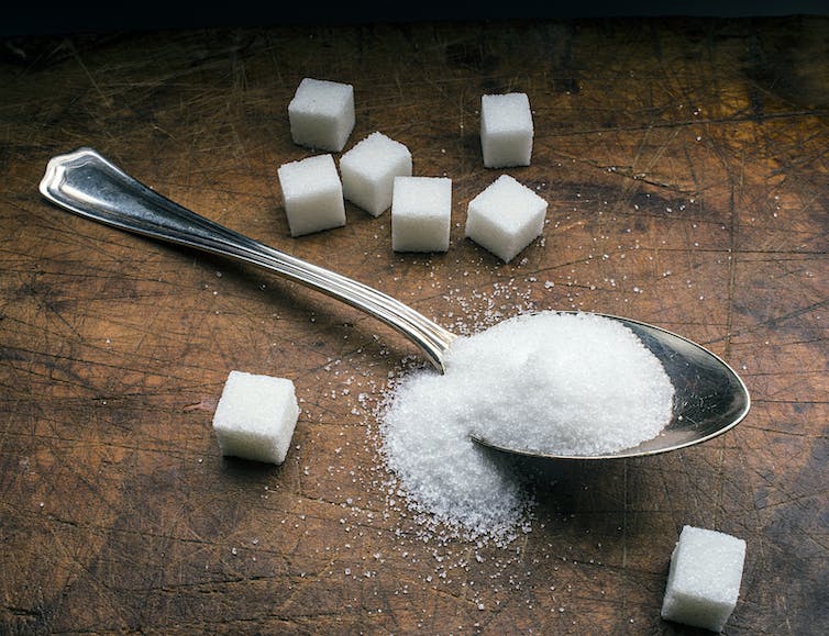 A spoonful of sugar, surrounded by sugar cubes, on a wooden table.