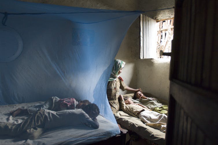 A woman strokes her child's head next to other sleeping under a bed net