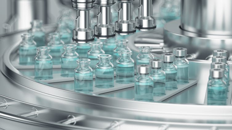 Glass vials arranged in a row move through a conveyer belt, where they are filled with the vaccine.