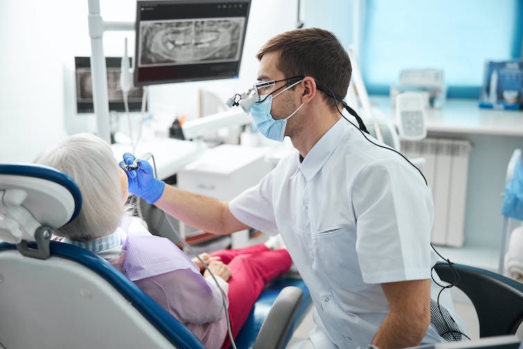 A male dentist performs a dental procedure on an older woman.