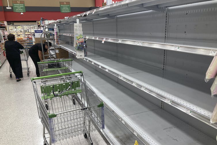 Bare shelves that once held bottled water in a store with shoppers.