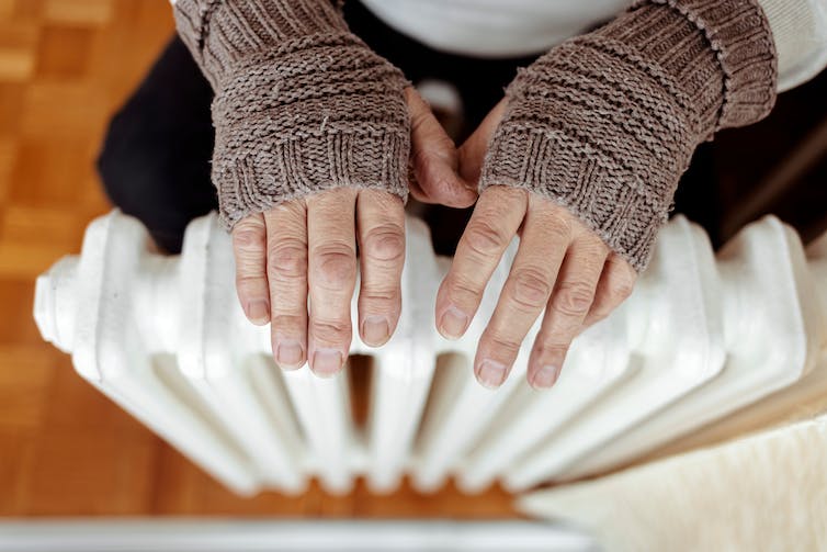 A person warms their hands on a radiator.
