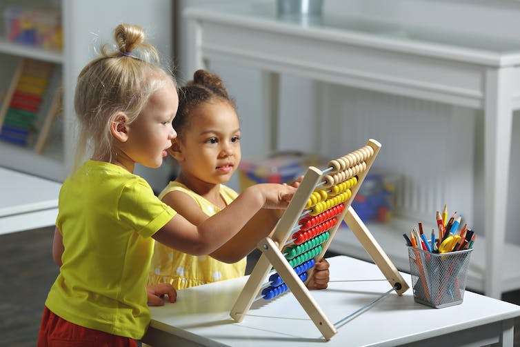 Two young girls play with an abacus at daycare or school together.