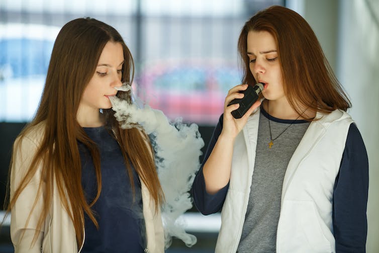 Two teenage girls smoking electronic cigarettes in a store.
