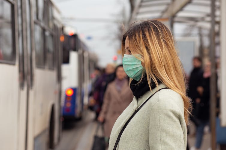 A woman at a bus station wearing a mask.