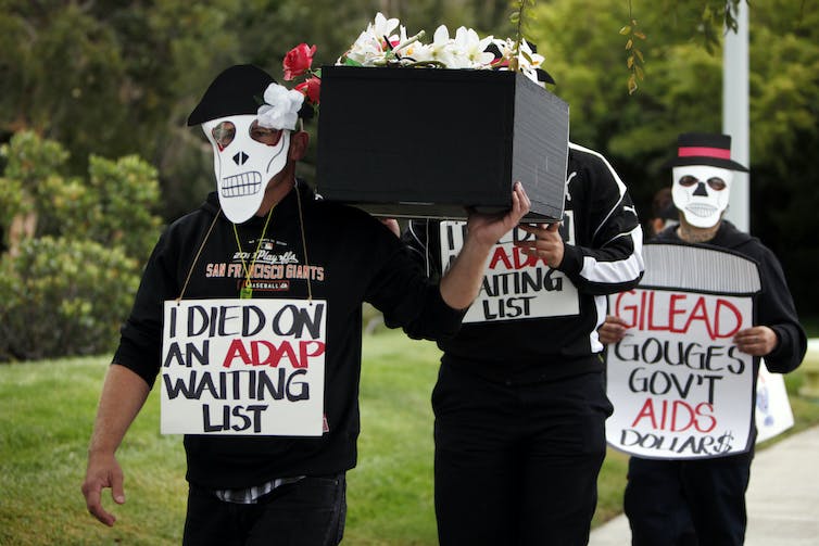 Protestors holding a black coffin, wearing paper skull masks and signs reading 'I died on an ADAP waiting list' and 'Gilead gouges gov' AIDS dollars'