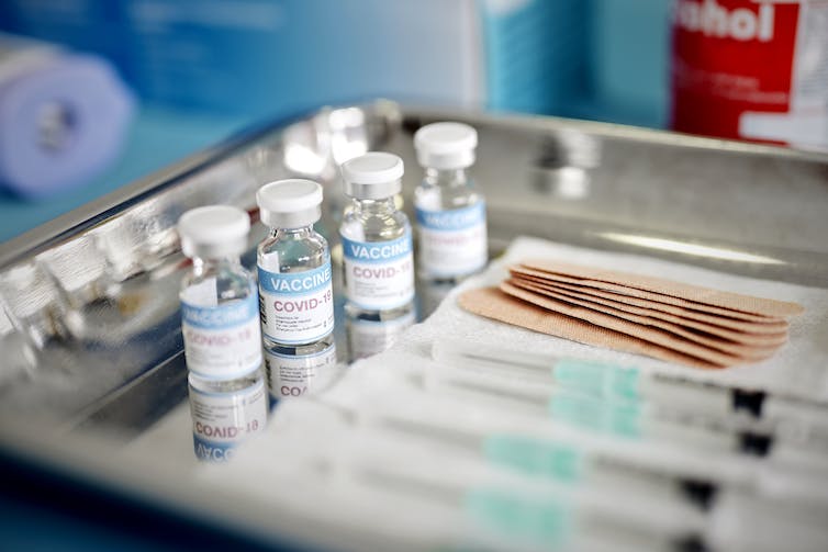 Vials and syringes containing COVID-19 vaccine are displayed on a tray.
