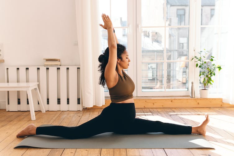 A pregnant woman doing the splits on a yoga mat.
