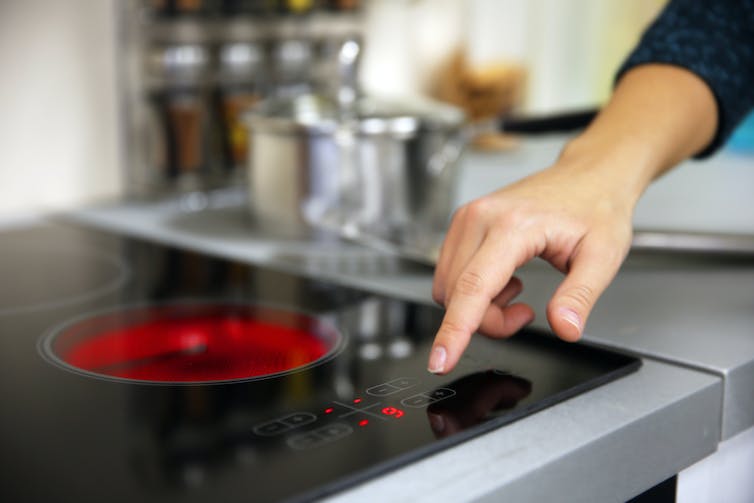A hand switches an electric hob on.