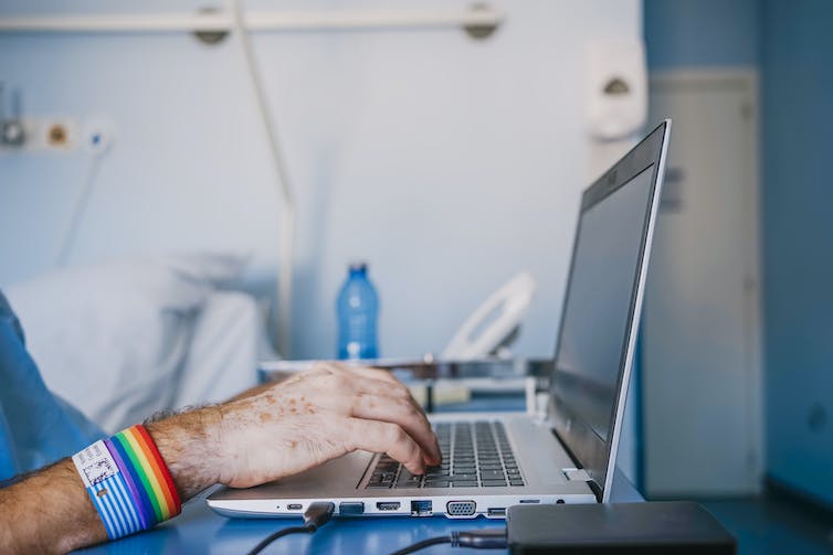Close-up of hands of patient using laptop, wearing rainbow band.