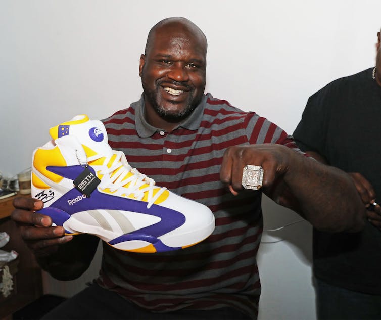 Man poses with large shoe and championship ring.