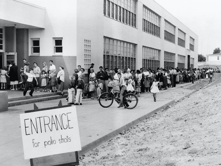 families in line outside a school with a sign 'Entrance for polio shots' in 1955