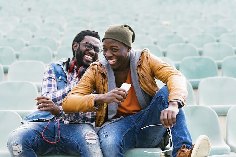 Two young men sitting in a stadium laughing together.