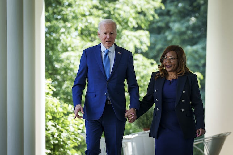 An elderly  white man is holding hands and walking with a black woman.