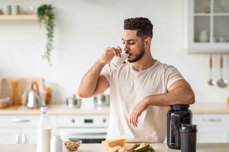 A man drink a glass of milk or protein shake in his kitchen.