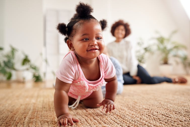 baby crawls toward camera with woman out of focus in background